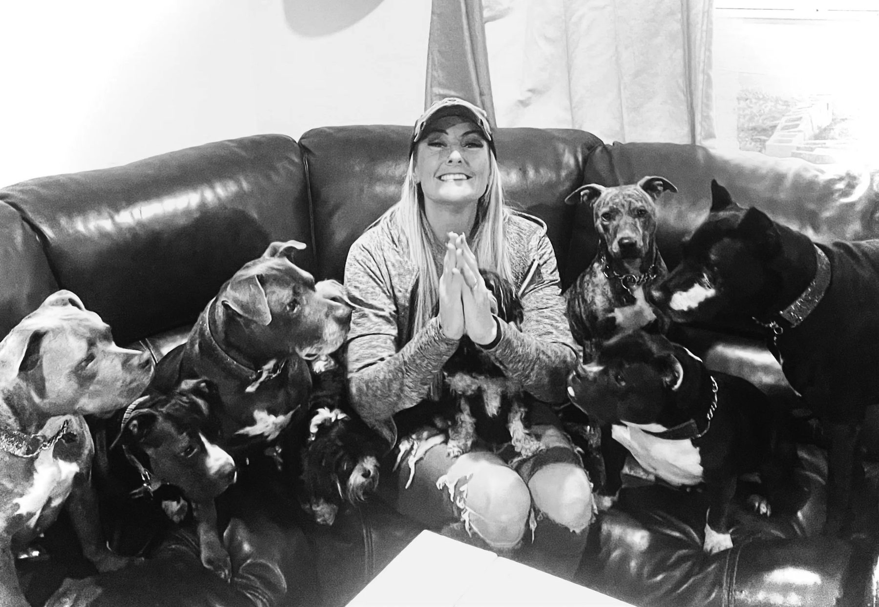 Black-and-white photo of Tiffany Skuraton, founder of Blue Waters Dog Rescue, on a couch surrounded by rescue dogs