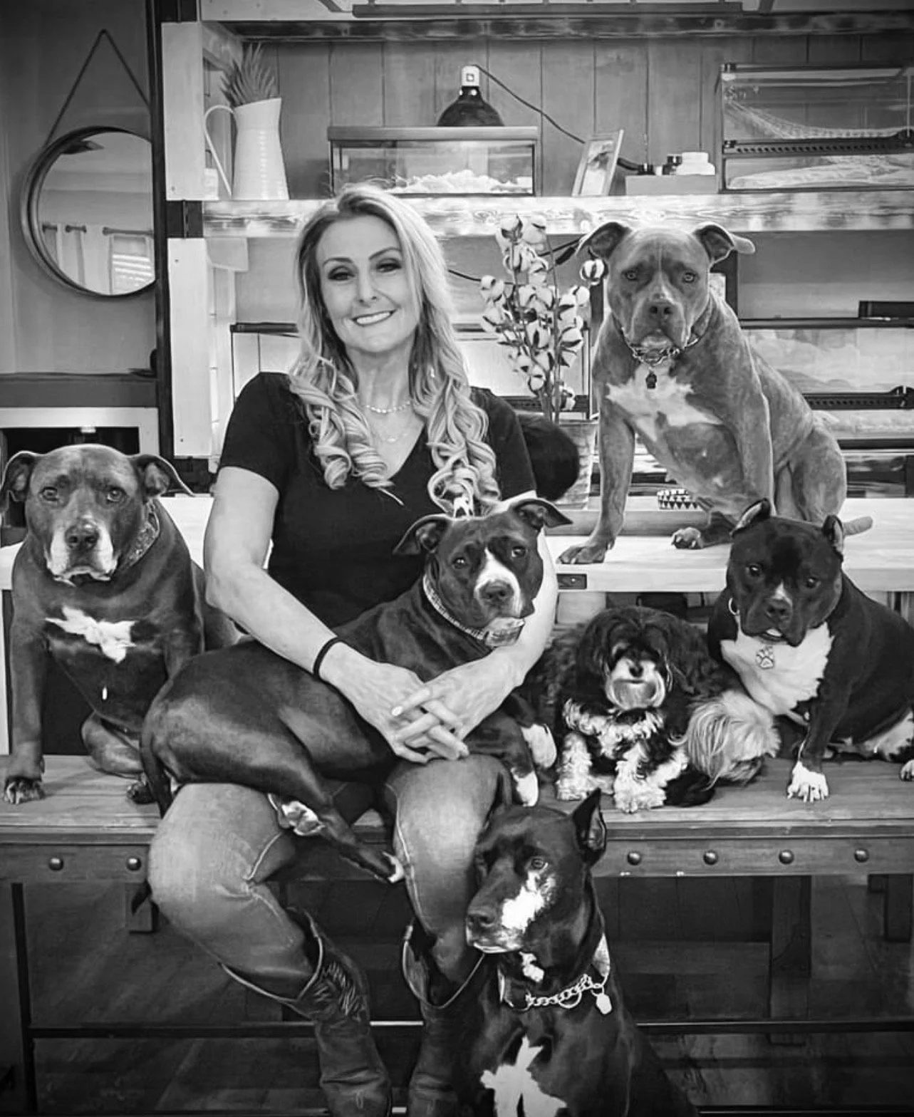 Black-and-white photo of a woman seated among several rescue dogs